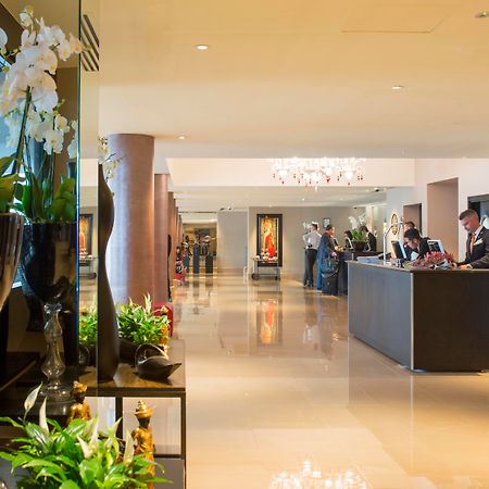 The May Fair, A Radisson Collection Hotel, Mayfair Londra Esterno foto The photo shows a spacious and elegantly designed hotel lobby. There are decorative elements such as flowers and plants along the sides, enhancing the luxurious atmosphere. In the background, you can see the reception area with staff members engaged 