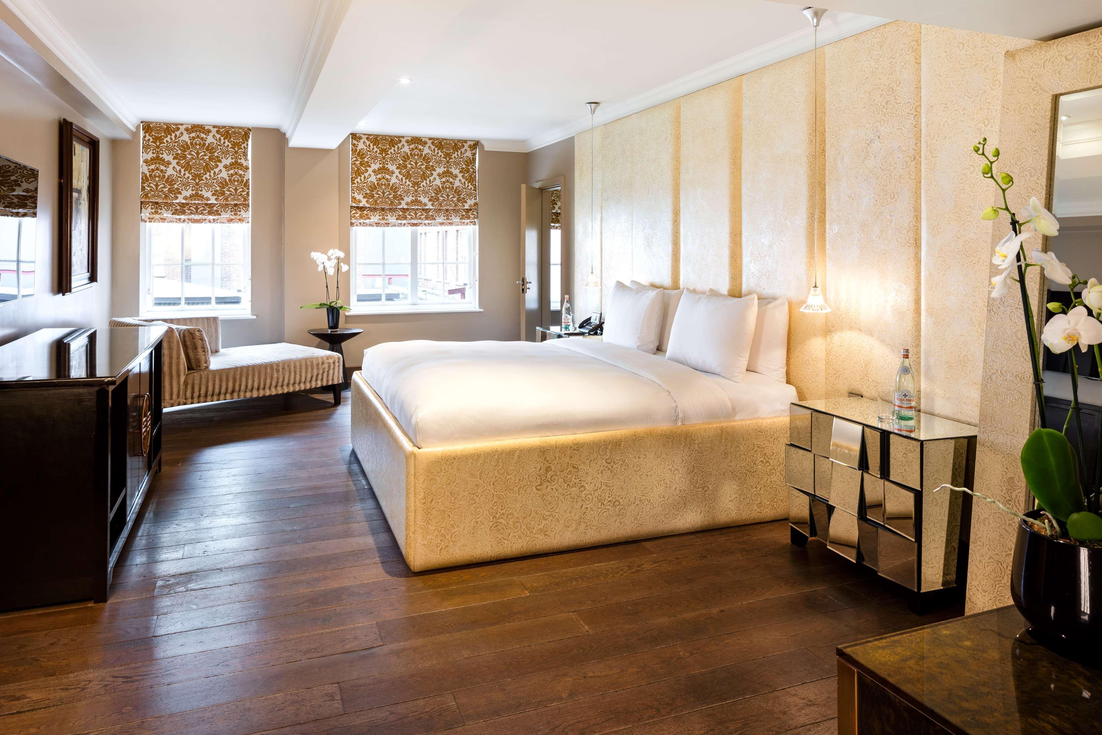 The May Fair, A Radisson Collection Hotel, Mayfair Londra Esterno foto The photo shows a modern and elegantly designed hotel room or bedroom. It features a large, plush bed with two pillows, situated against a light-colored wall. To one side, there is a stylish bench or chaise lounge, adding a comfortable seating area. 