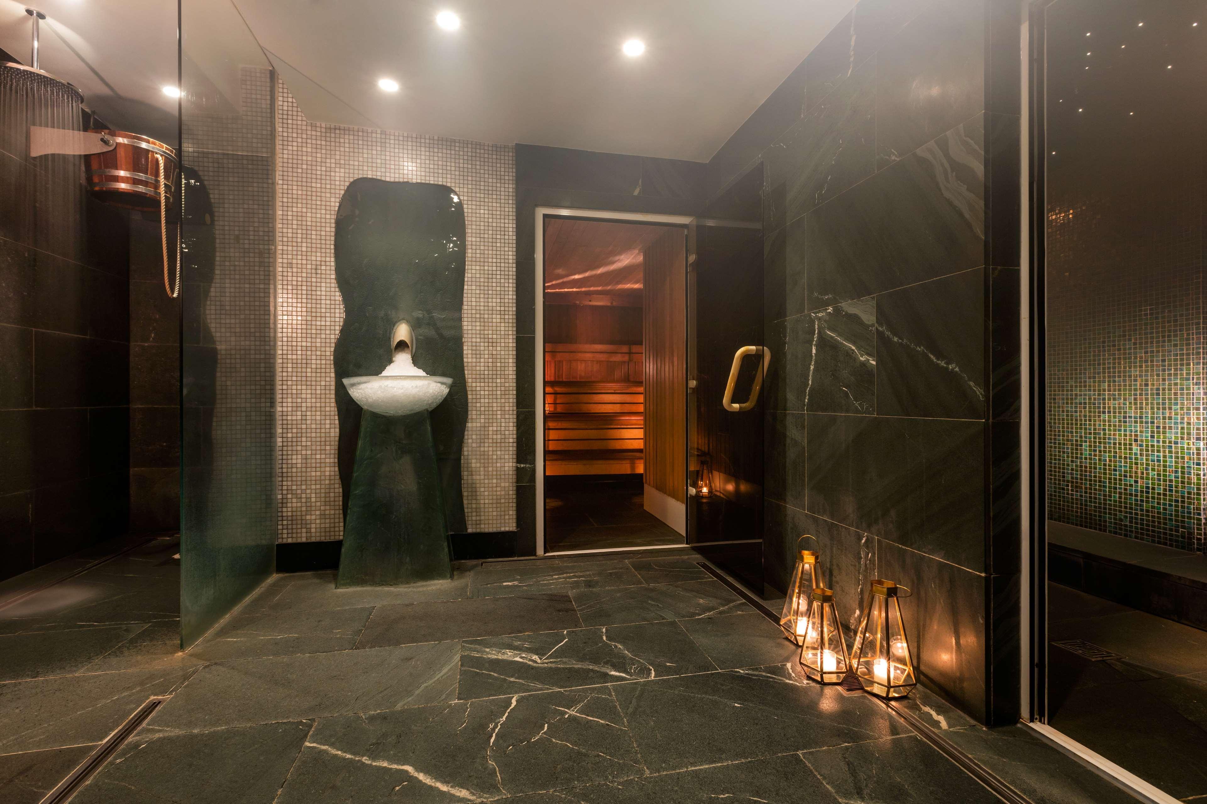 The May Fair, A Radisson Collection Hotel, Mayfair Londra Esterno foto The photo shows a modern and stylish bathroom or spa area. It features dark marble flooring and walls with a sleek design. On one side, there is a unique sink that has an artistic shape, mounted on the wall. Next to the sink, there is a glass door th