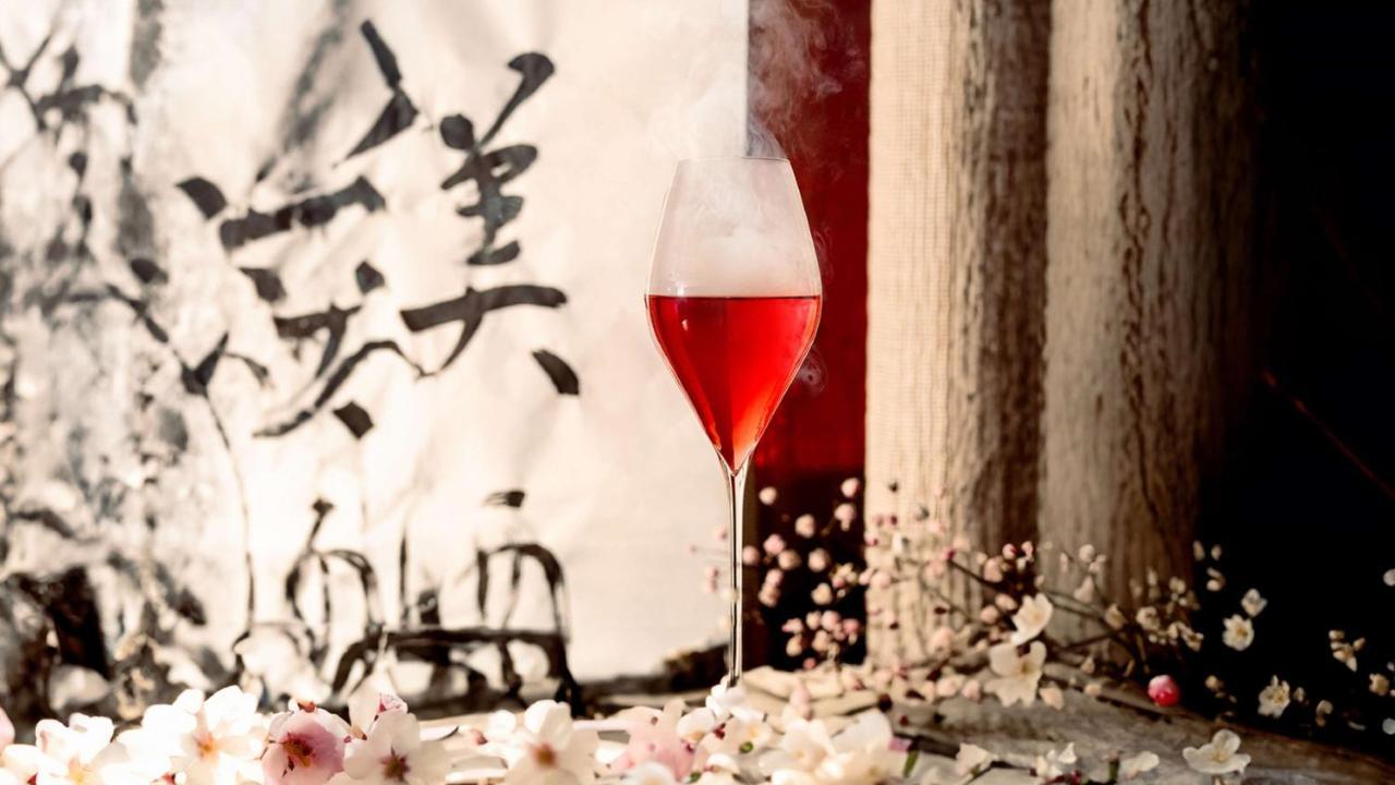 The May Fair, A Radisson Collection Hotel, Mayfair Londra Esterno foto The photo features a glass of red beverage, elegantly presented in a stemmed glass. The drink emits a mist, adding an ethereal quality to the image. Surrounding the glass are delicate pink flowers, enhancing the aesthetic appeal. In the background, t