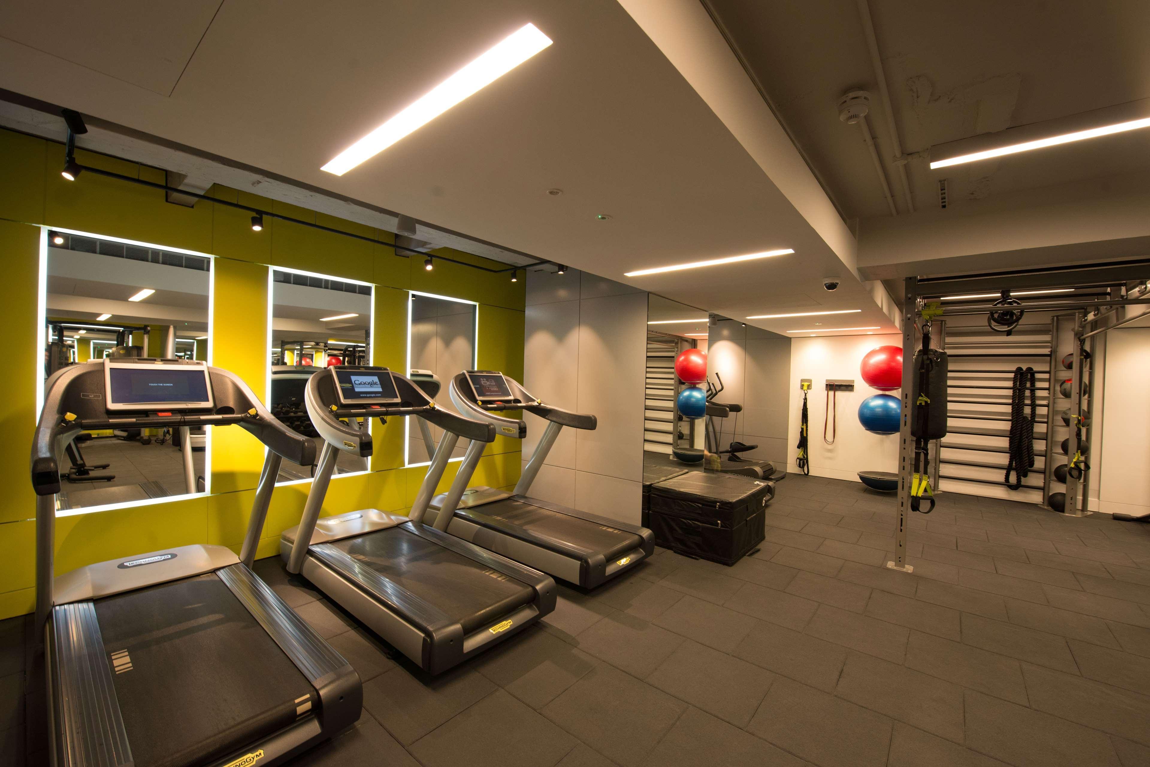 The May Fair, A Radisson Collection Hotel, Mayfair Londra Esterno foto The photo shows a modern gym interior featuring several exercise equipment. In the foreground, there are three treadmills aligned along a wall with mirrors. The wall behind the treadmills is painted a vibrant green, enhancing the energetic atmosphere