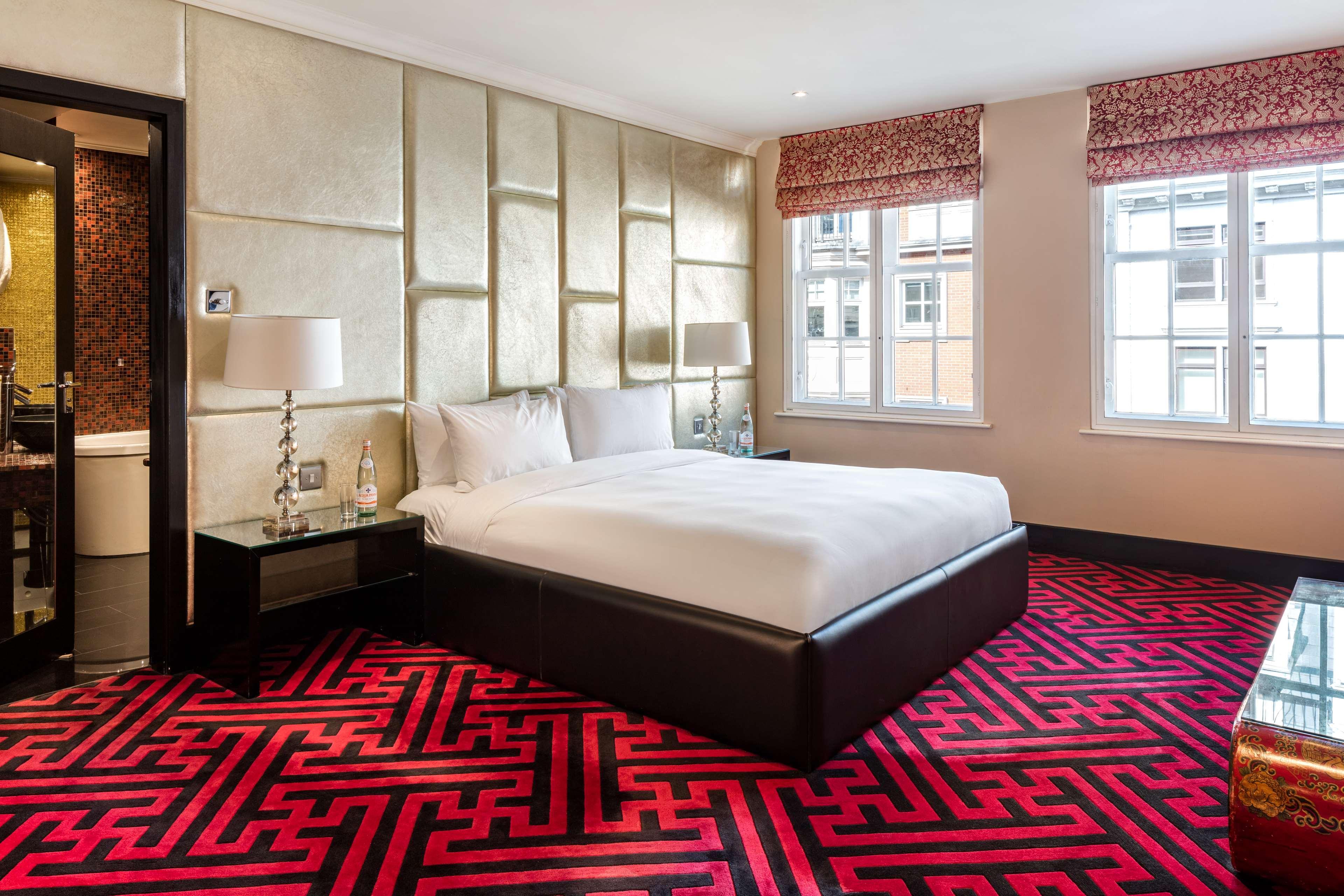 The May Fair, A Radisson Collection Hotel, Mayfair Londra Esterno foto The photo shows a modern hotel room featuring a large bed with white bedding. The walls are accented with a stylish, textured design, and the room is illuminated by natural light coming from two windows, which have patterned blinds. The floor is cove