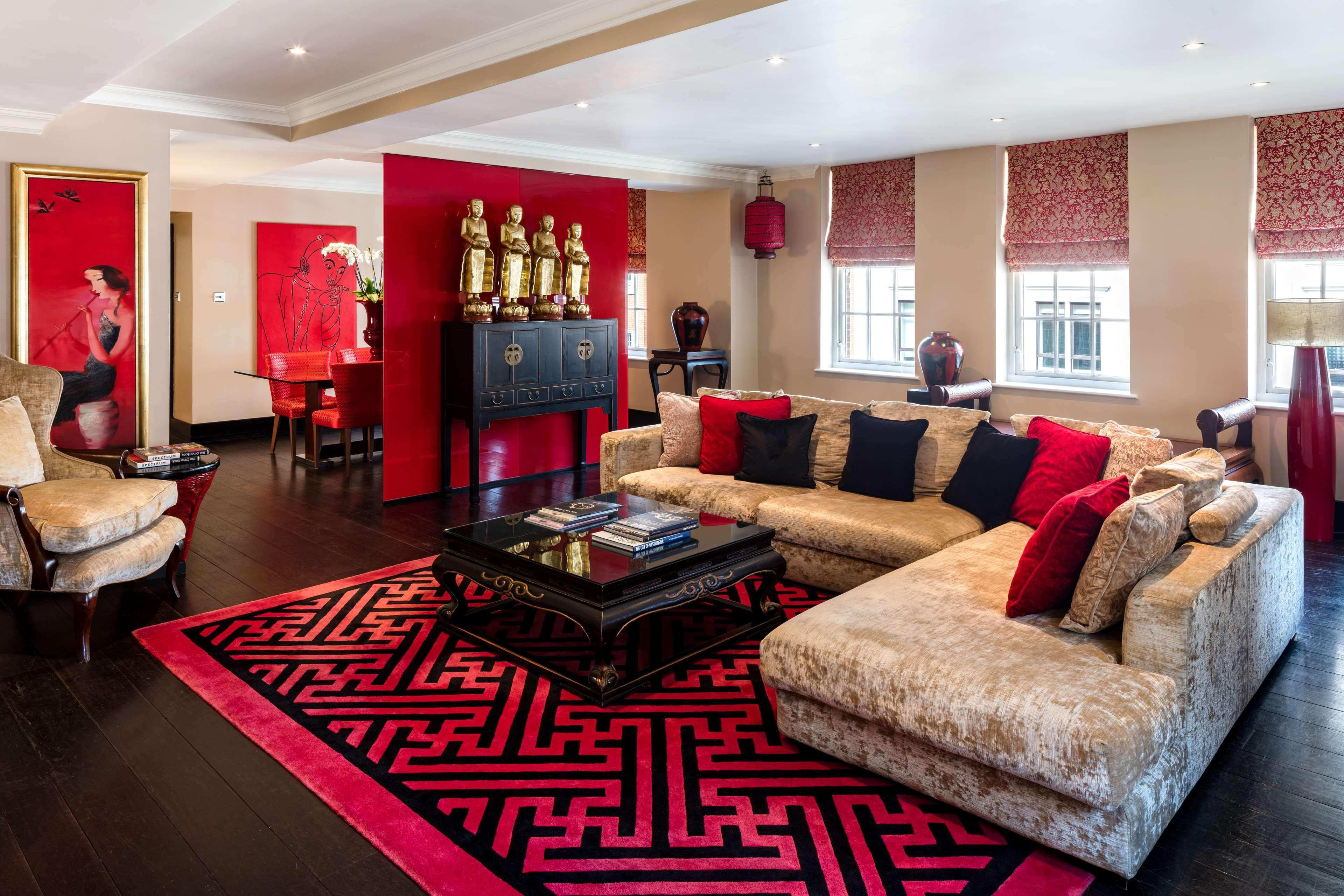 The May Fair, A Radisson Collection Hotel, Mayfair Londra Esterno foto The photo shows a stylish and elegant living room designed with a modern aesthetic. The space features a large, plush sofa in a light color, complemented by red and black throw pillows. A dark coffee table sits in the center, adorned with books and d