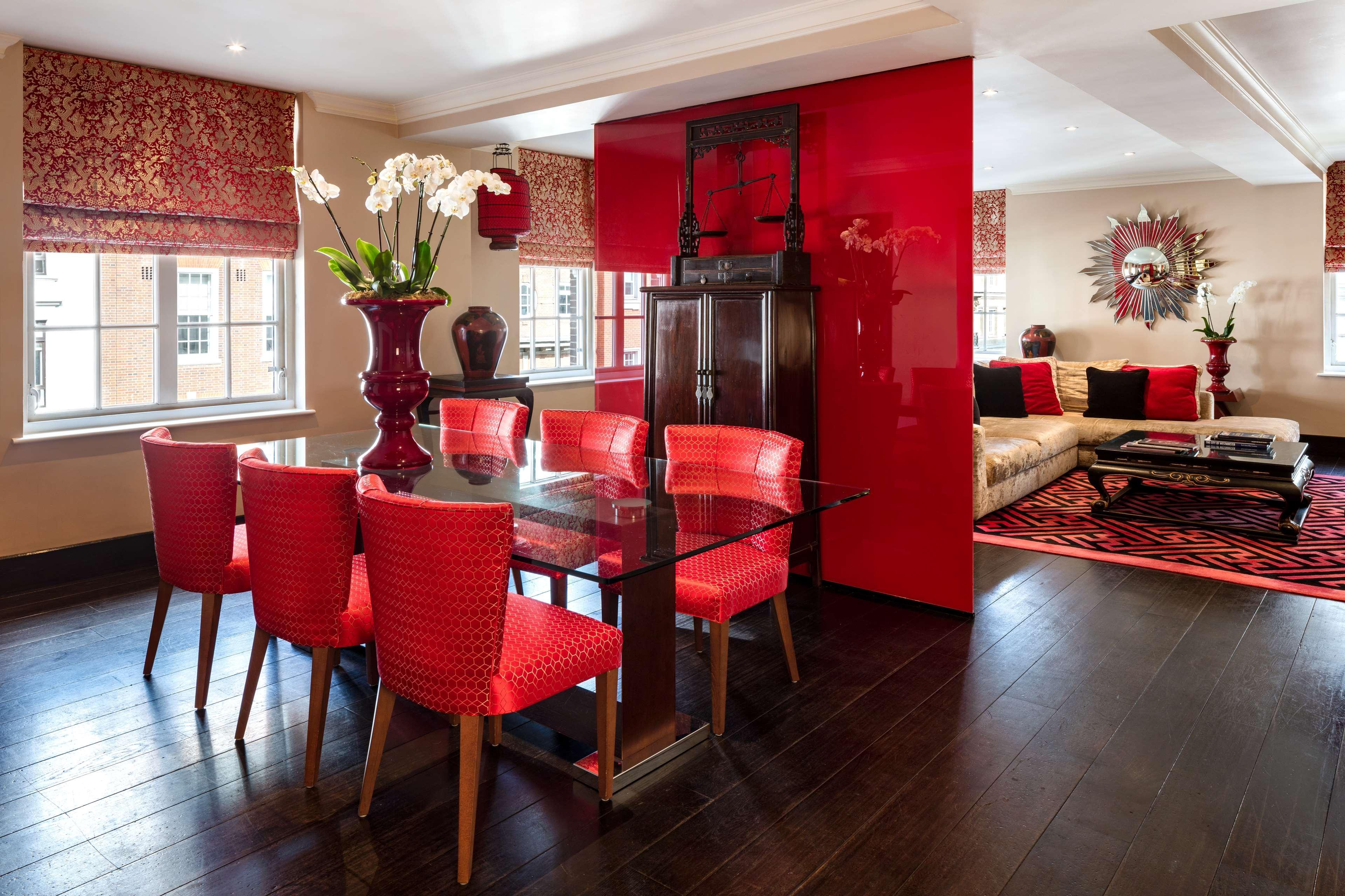 The May Fair, A Radisson Collection Hotel, Mayfair Londra Esterno foto The photo depicts a stylish, modern living and dining area. 

- **Dining Area**: There is a glass dining table with six vibrant red chairs surrounding it. A large vase containing white orchids sits at the center of the table.
  
- **Decor Elements**: