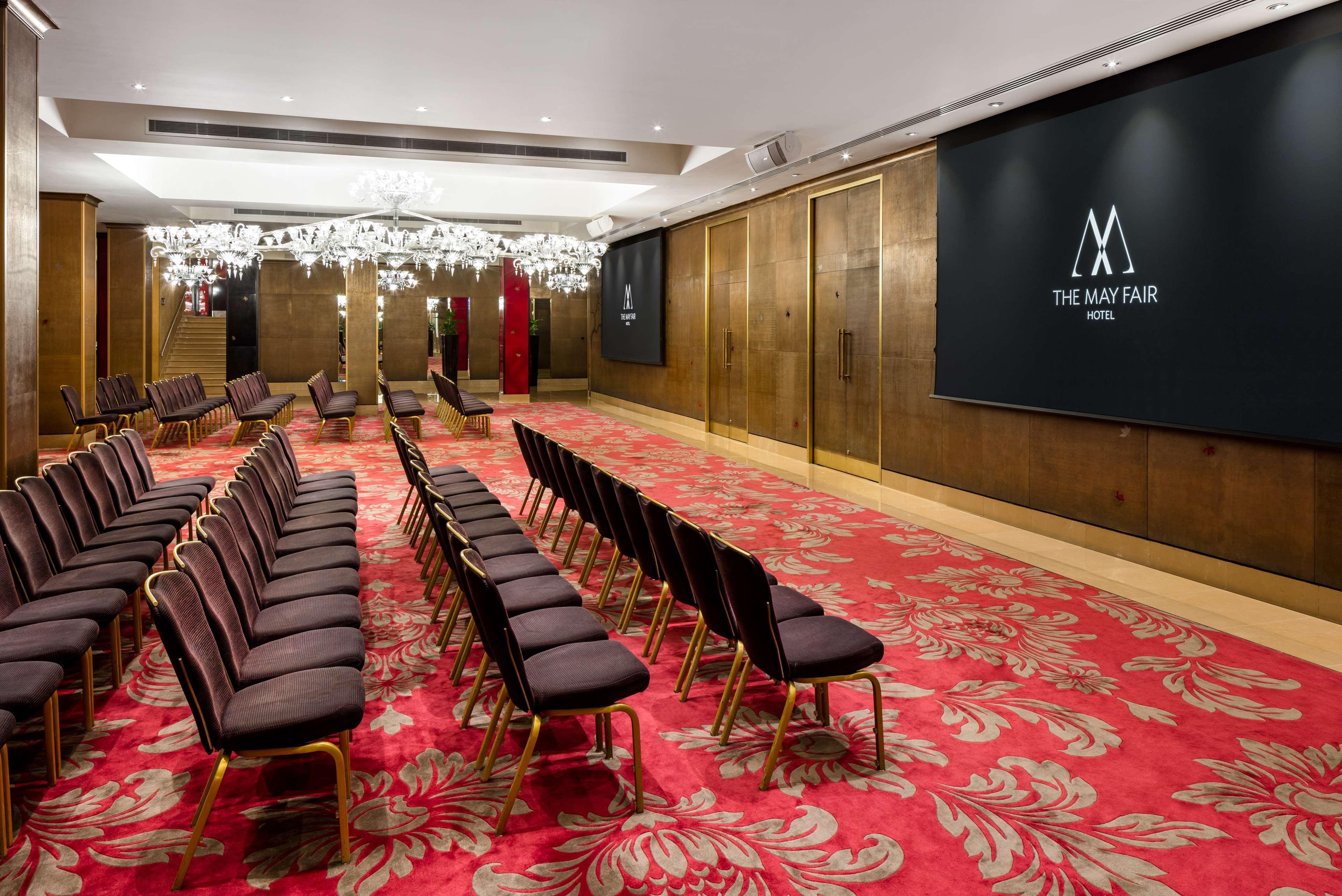 The May Fair, A Radisson Collection Hotel, Mayfair Londra Esterno foto The photo shows a conference or event room inside The May Fair Hotel. The space has a stylish design with decorative chandeliers hanging from the ceiling. There are rows of upholstered seating arranged in front of a large screen that displays the hot