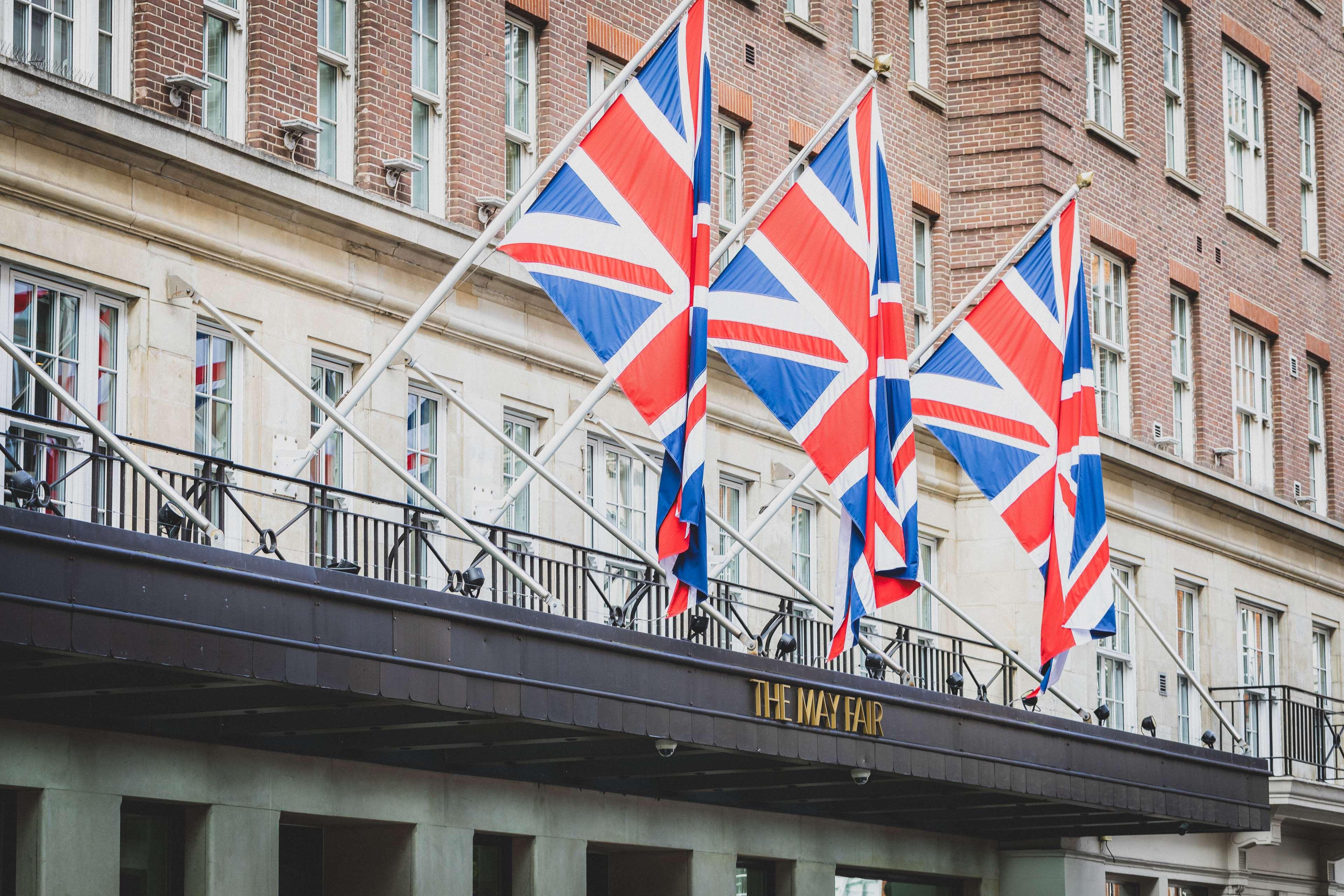 The May Fair, A Radisson Collection Hotel, Mayfair Londra Esterno foto The photo shows a building façade with several Union Jack flags prominently displayed. These flags are arranged in a row, indicating a British theme. The entrance of the building features a sign with the name "The Mayfair," suggesting that this could