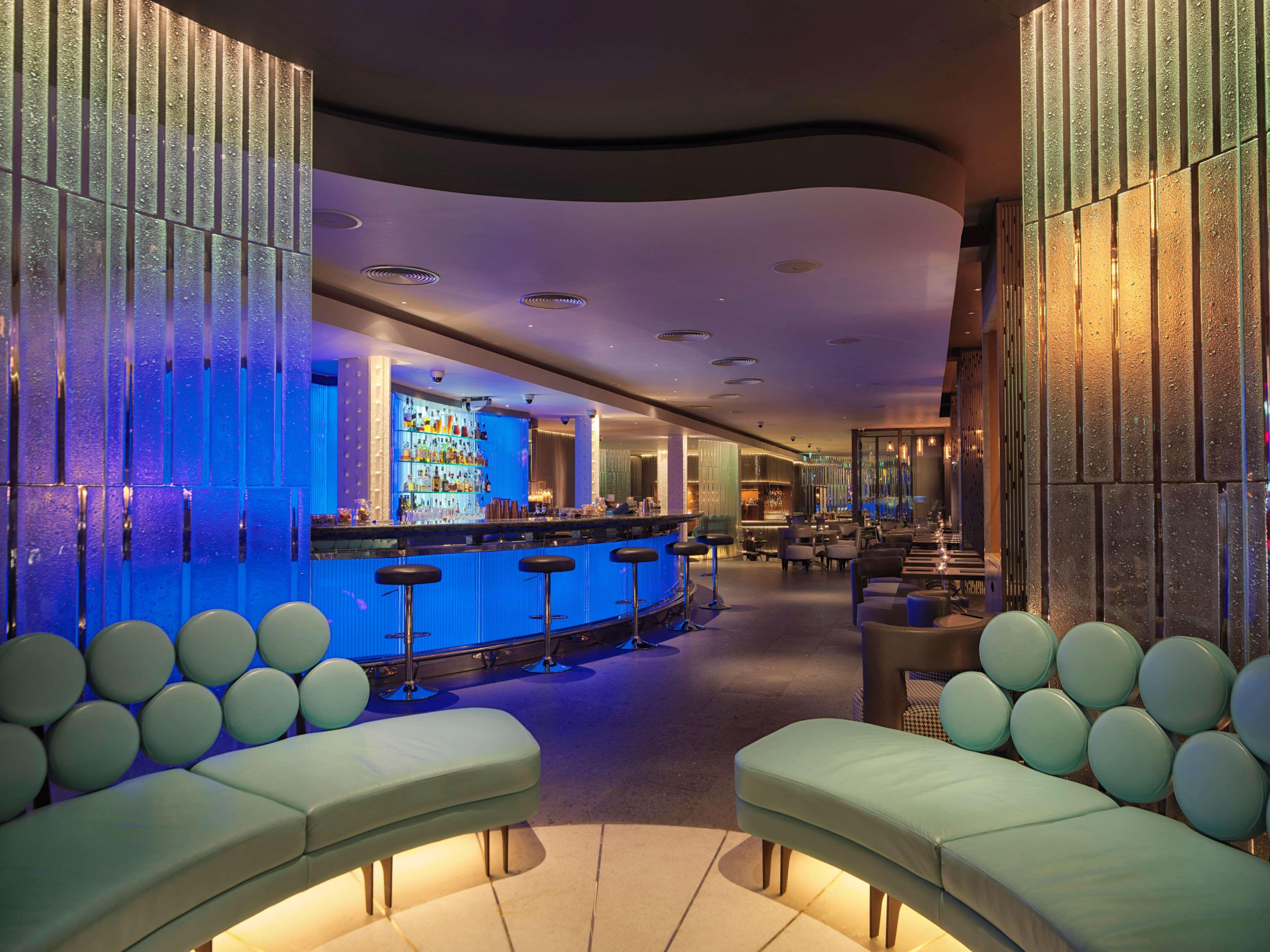 The May Fair, A Radisson Collection Hotel, Mayfair Londra Esterno foto The photo shows a modern bar or lounge area with a stylish and contemporary design. The interior features curved seating with light green upholstery, creating a relaxed atmosphere. Behind the seating, there is a bar area illuminated with blue lightin