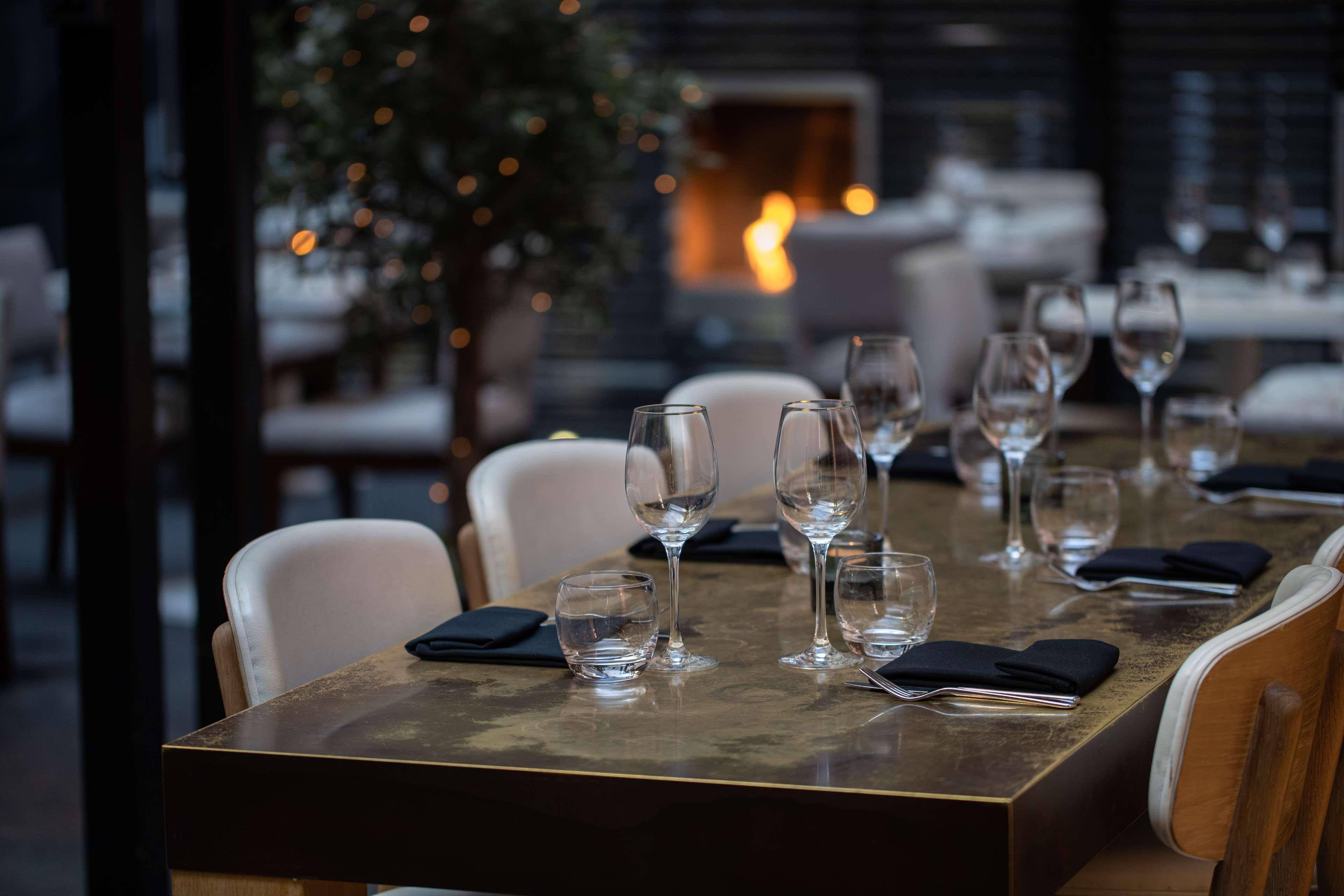 The May Fair, A Radisson Collection Hotel, Mayfair Londra Esterno foto The photo shows a stylish restaurant dining area. A beautifully set table is in the foreground, featuring elegant glassware and black napkins. The table has a glossy surface and appears to be well-prepared for dining. In the background, there is a co