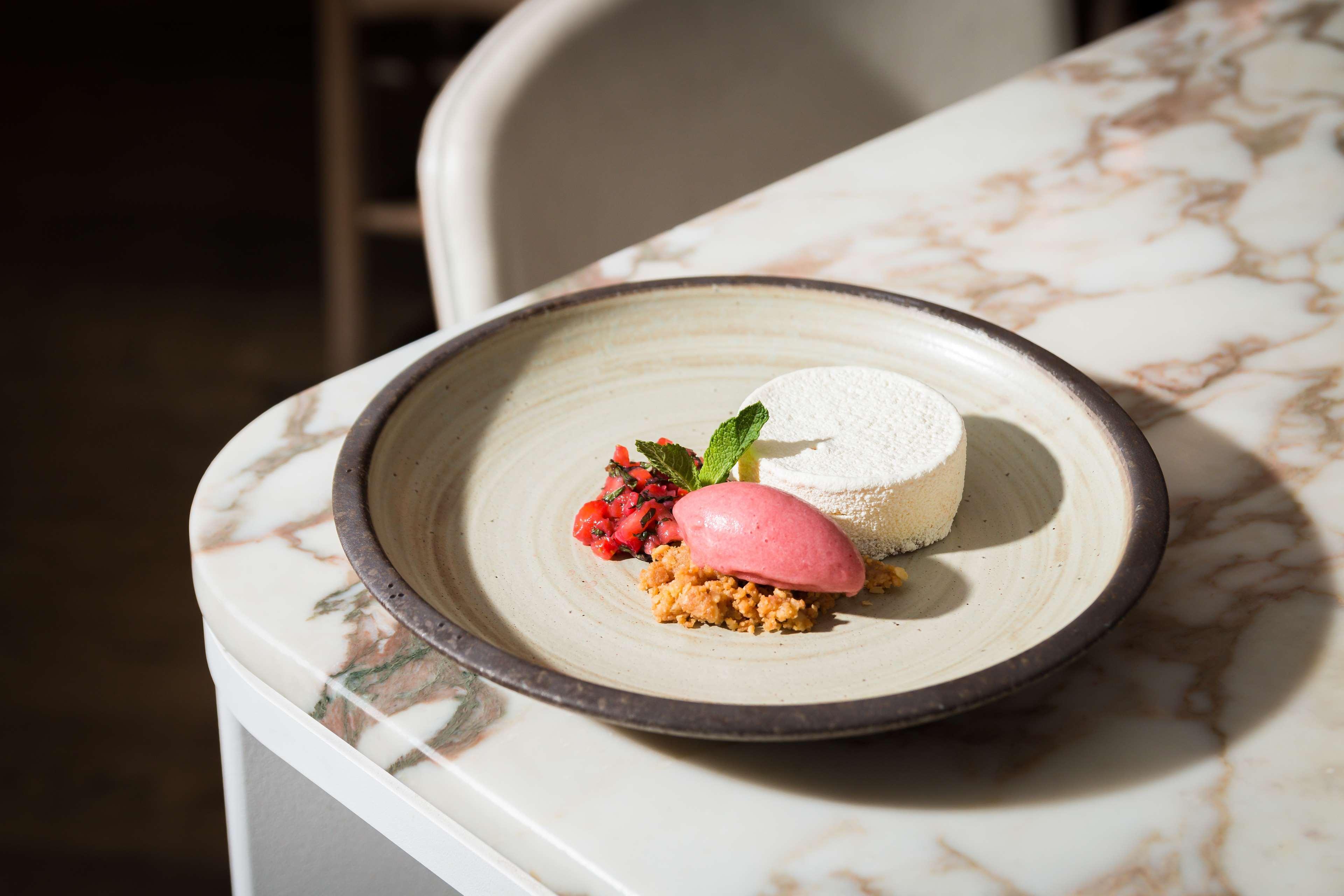 The May Fair, A Radisson Collection Hotel, Mayfair Londra Esterno foto The photo showcases a beautifully plated dessert on a round, light-colored plate. The dessert features a cylindrical piece of creamy white mousse or panna cotta, accompanied by a vibrant pink scoop of sorbet. There is also a small portion of crumbled