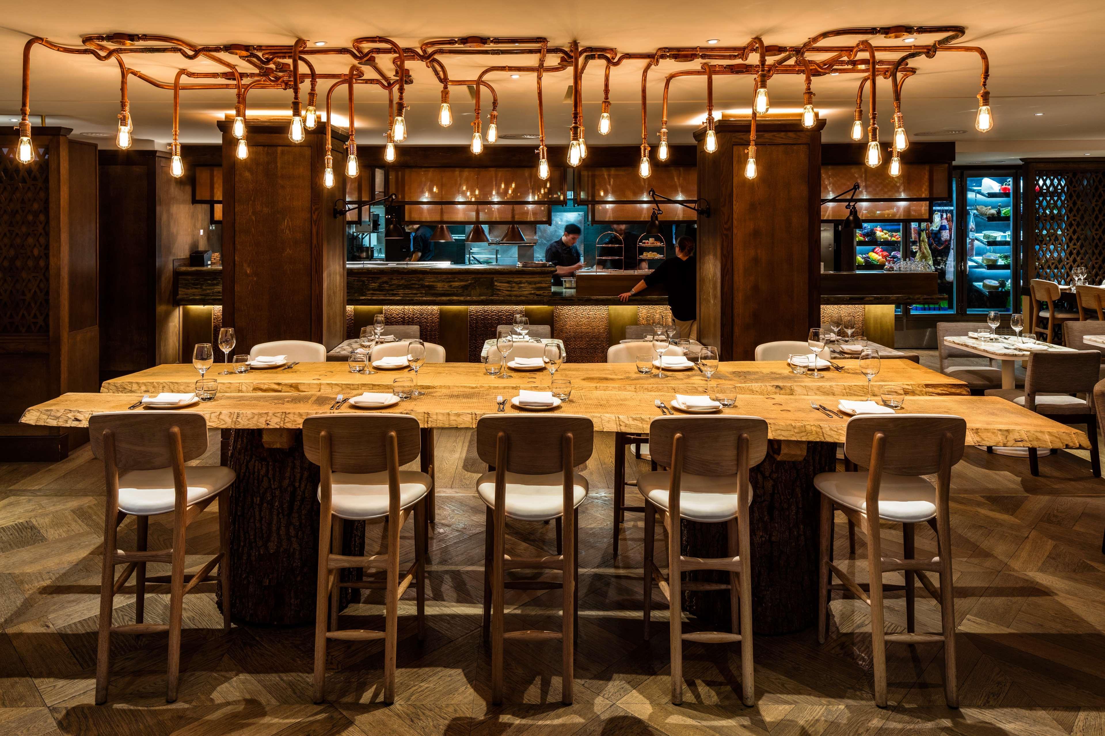 The May Fair, A Radisson Collection Hotel, Mayfair Londra Esterno foto The photo shows a stylish restaurant interior. There is a large, rustic wooden dining table with several white chairs around it, suggesting a communal dining experience. Above the table, unique light fixtures made of twisted branches and hanging bulb