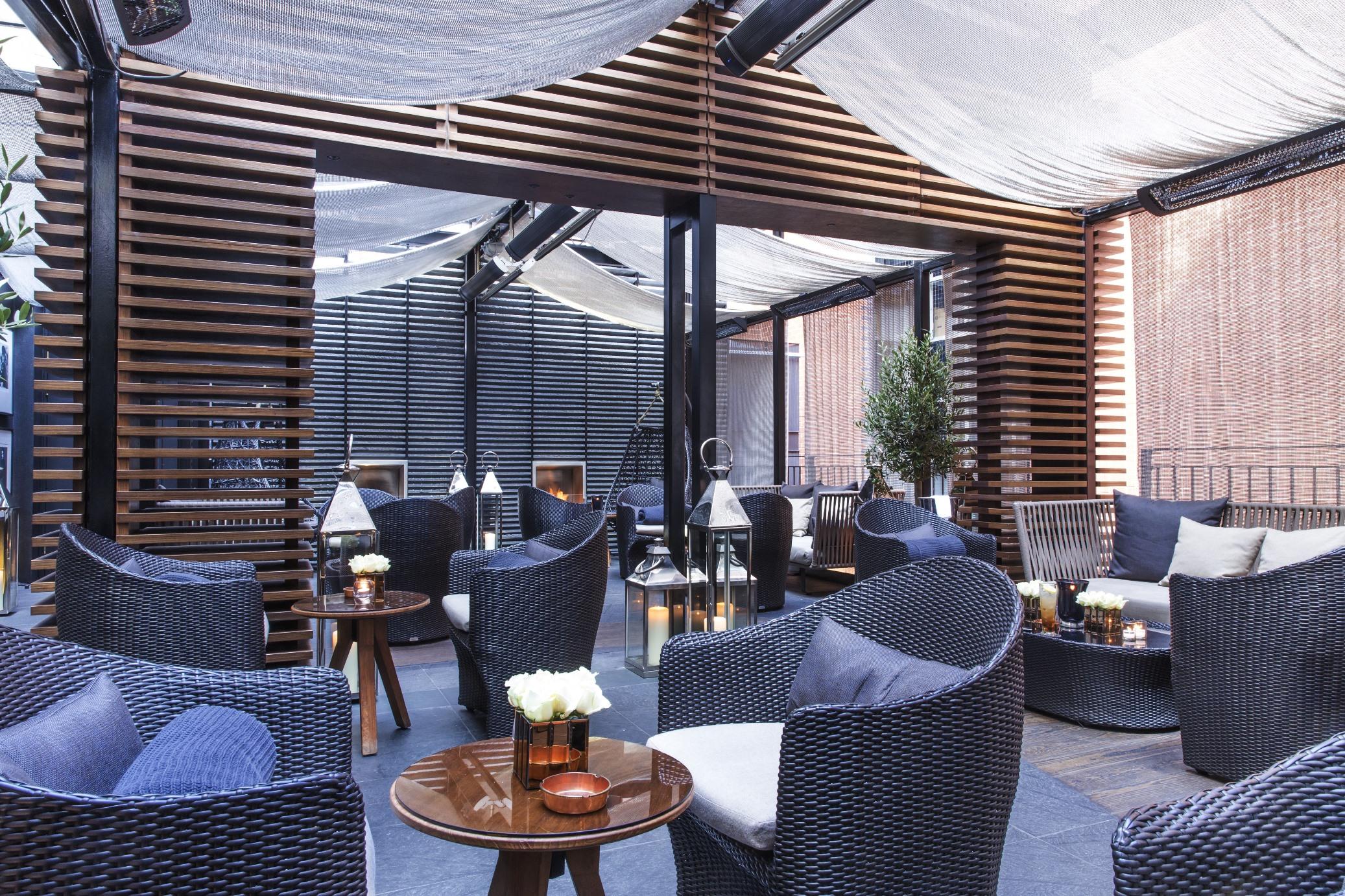 The May Fair, A Radisson Collection Hotel, Mayfair Londra Esterno foto The photo showcases a stylish indoor lounge area with modern decor. It features a series of comfortable wicker armchairs arranged around wooden tables. The space is adorned with elegant touches like small vases containing flowers on the tables. The c