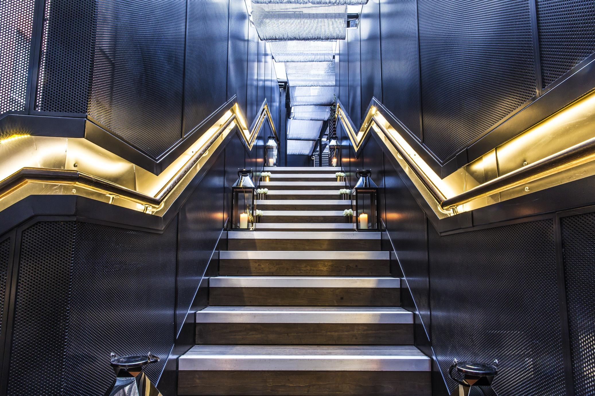 The May Fair, A Radisson Collection Hotel, Mayfair Londra Esterno foto The photo depicts a staircase with a modern and sleek design. The steps are a combination of metal and wood, creating a stylish contrast. The walls on either side of the staircase are characterized by a textured, dark material, with zigzag-shaped lig