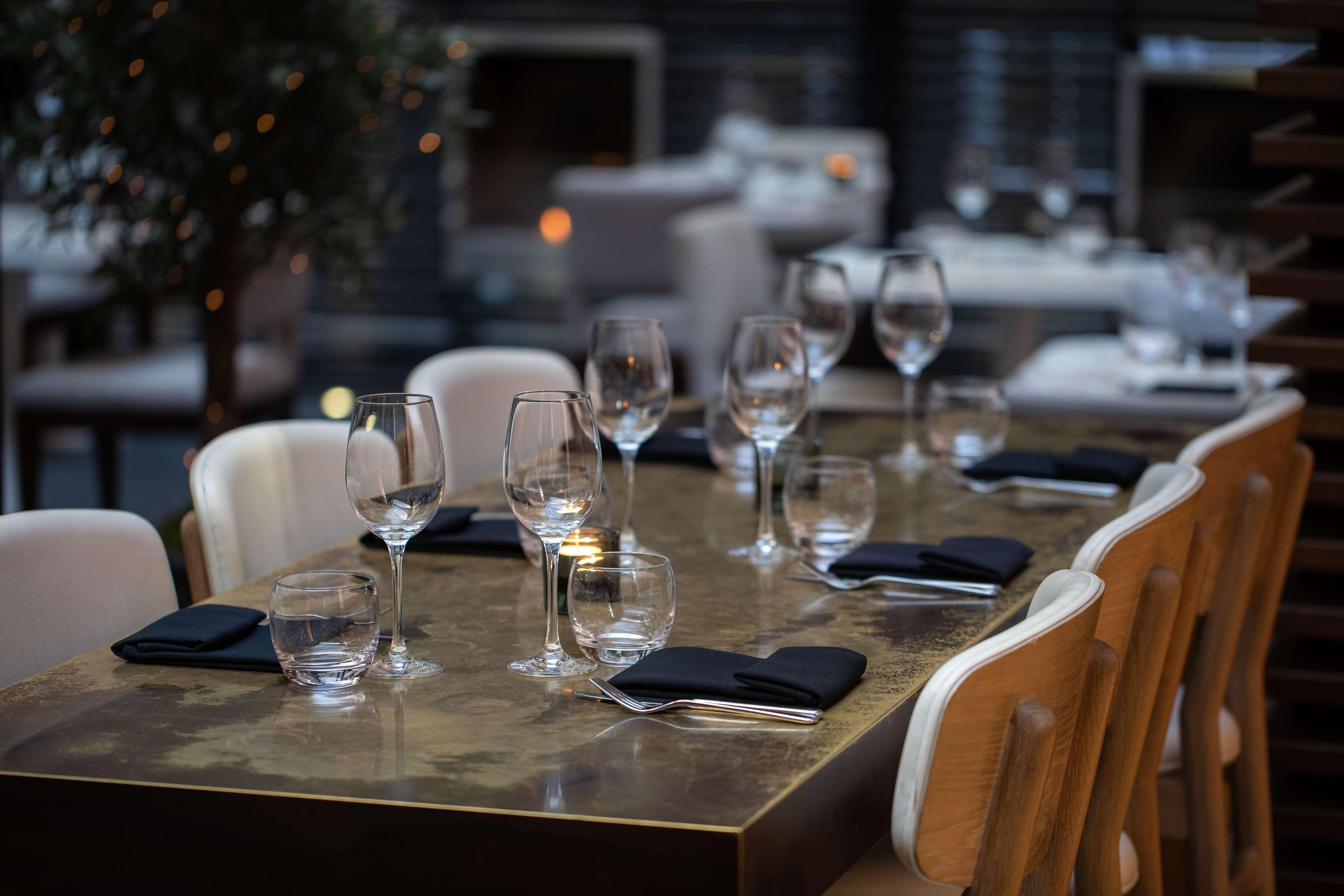 The May Fair, A Radisson Collection Hotel, Mayfair Londra Esterno foto The photo shows a dining table set for a meal. The table is made of a dark, polished material and has several place settings. Each setting features a wine glass, a smaller glass, and a neatly folded black napkin. The atmosphere appears elegant, with 