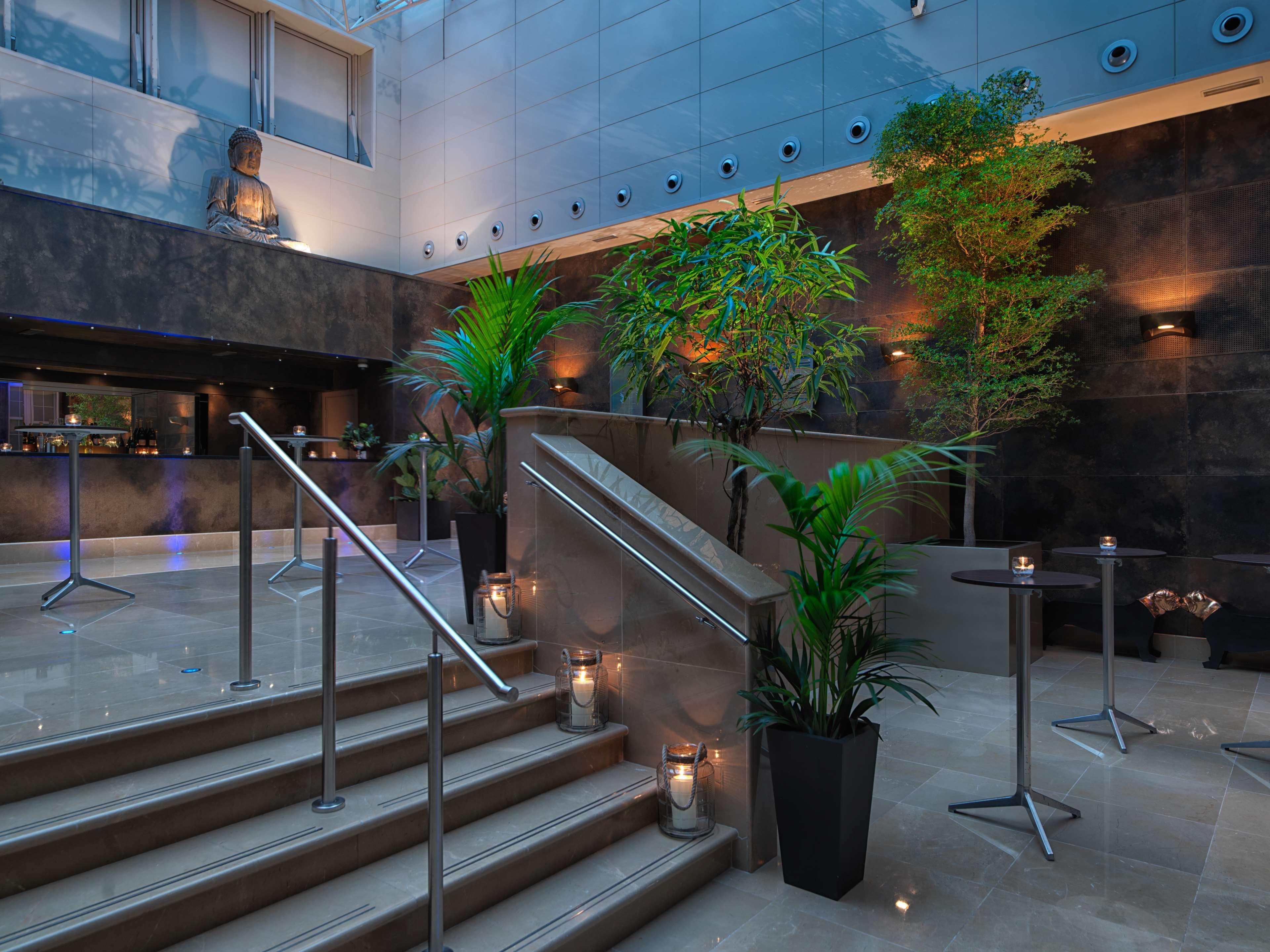 The May Fair, A Radisson Collection Hotel, Mayfair Londra Esterno foto The photo depicts a modern interior space, likely from a hotel or upscale venue. There is a stylish staircase leading upwards, flanked by decorative plants that add a touch of greenery to the environment. Soft lighting highlights the design elements,