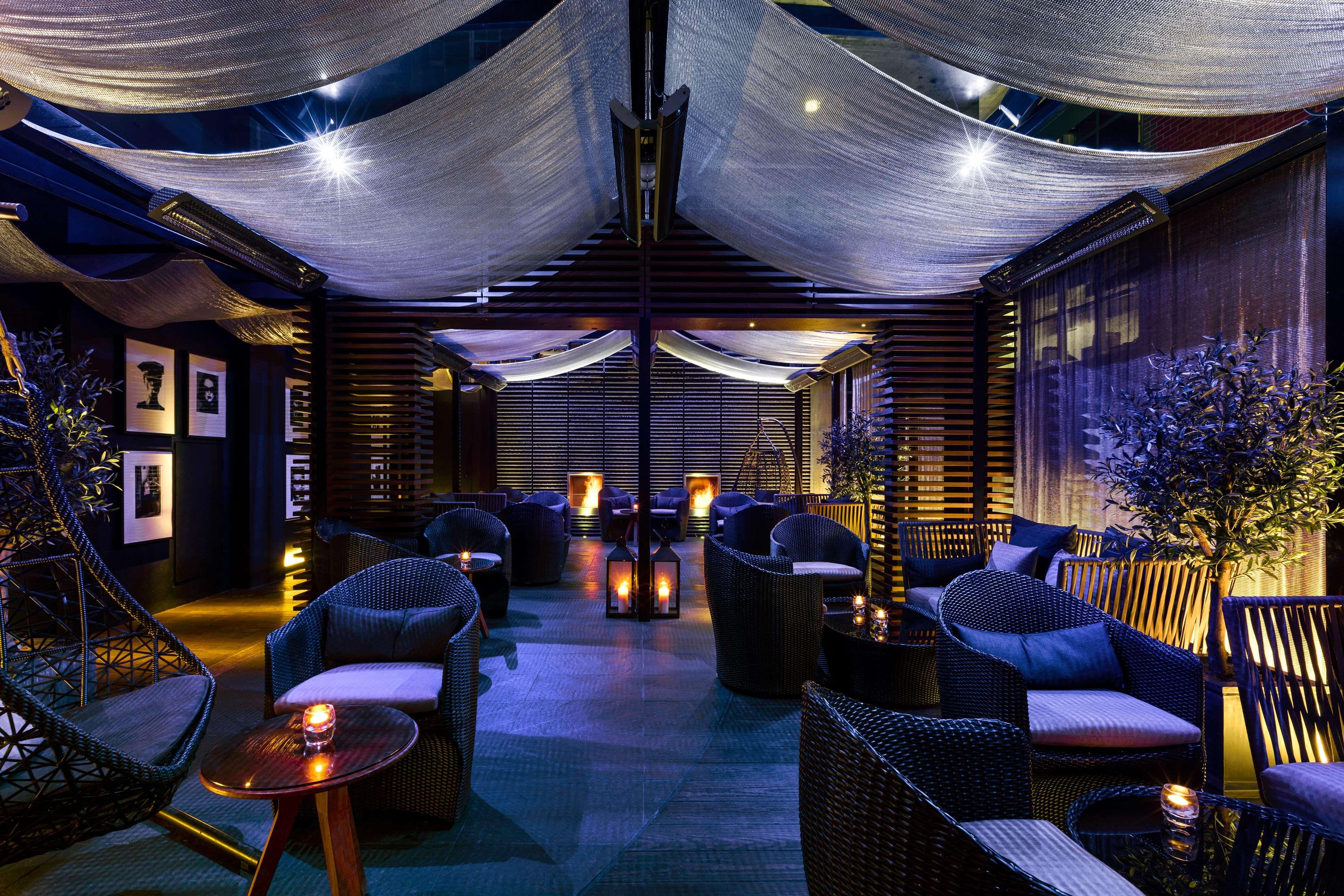 The May Fair, A Radisson Collection Hotel, Mayfair Londra Esterno foto The image depicts a stylish lounge area with a cozy and contemporary design. Soft, ambient lighting creates a relaxed atmosphere, complemented by draped fabric overhead. The space features comfortable seating, including wicker chairs and small tables