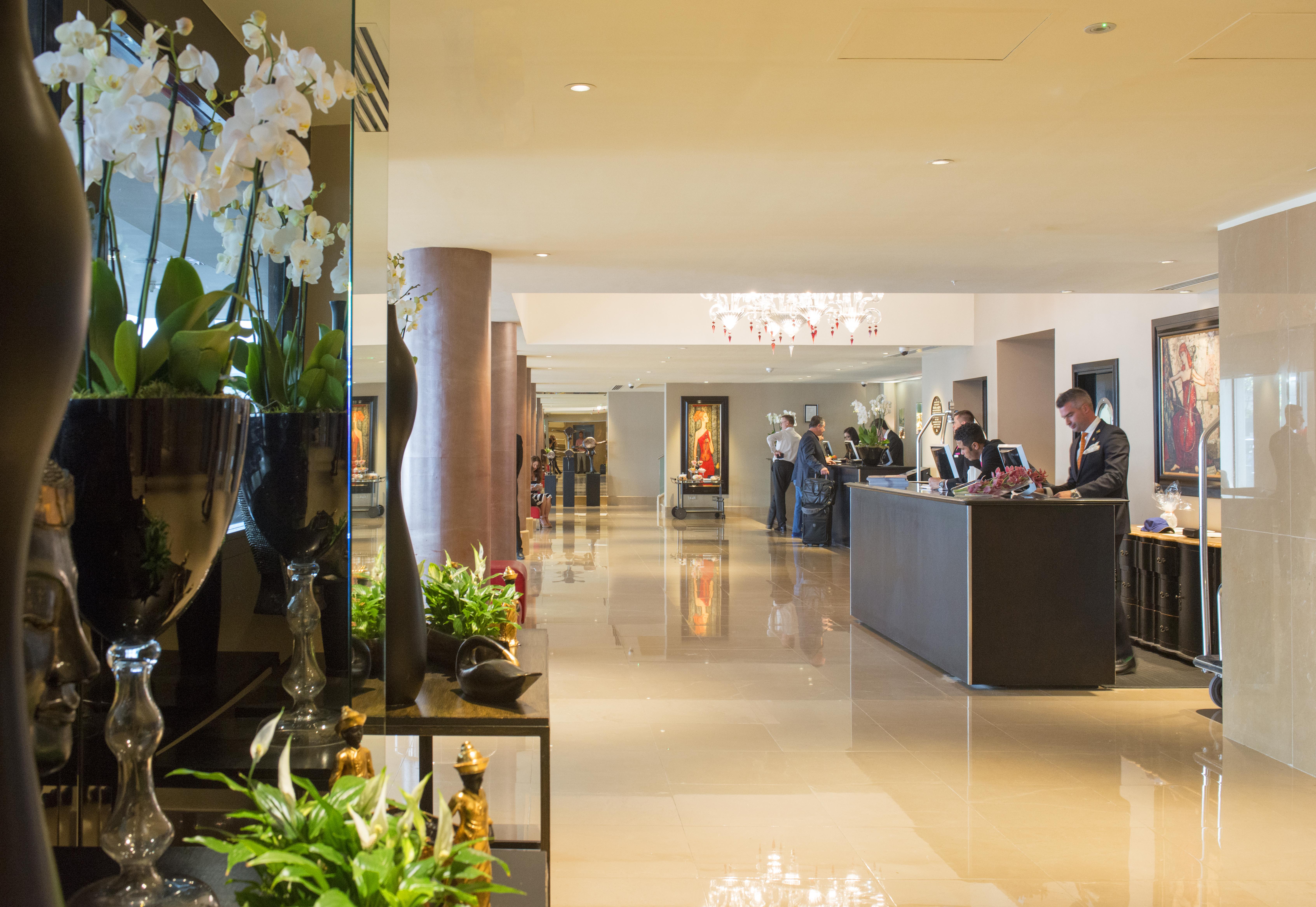 The May Fair, A Radisson Collection Hotel, Mayfair Londra Esterno foto The photo shows a spacious and elegantly designed hotel lobby. There are decorative elements such as flowers and plants along the sides, enhancing the luxurious atmosphere. In the background, you can see the reception area with staff members engaged 