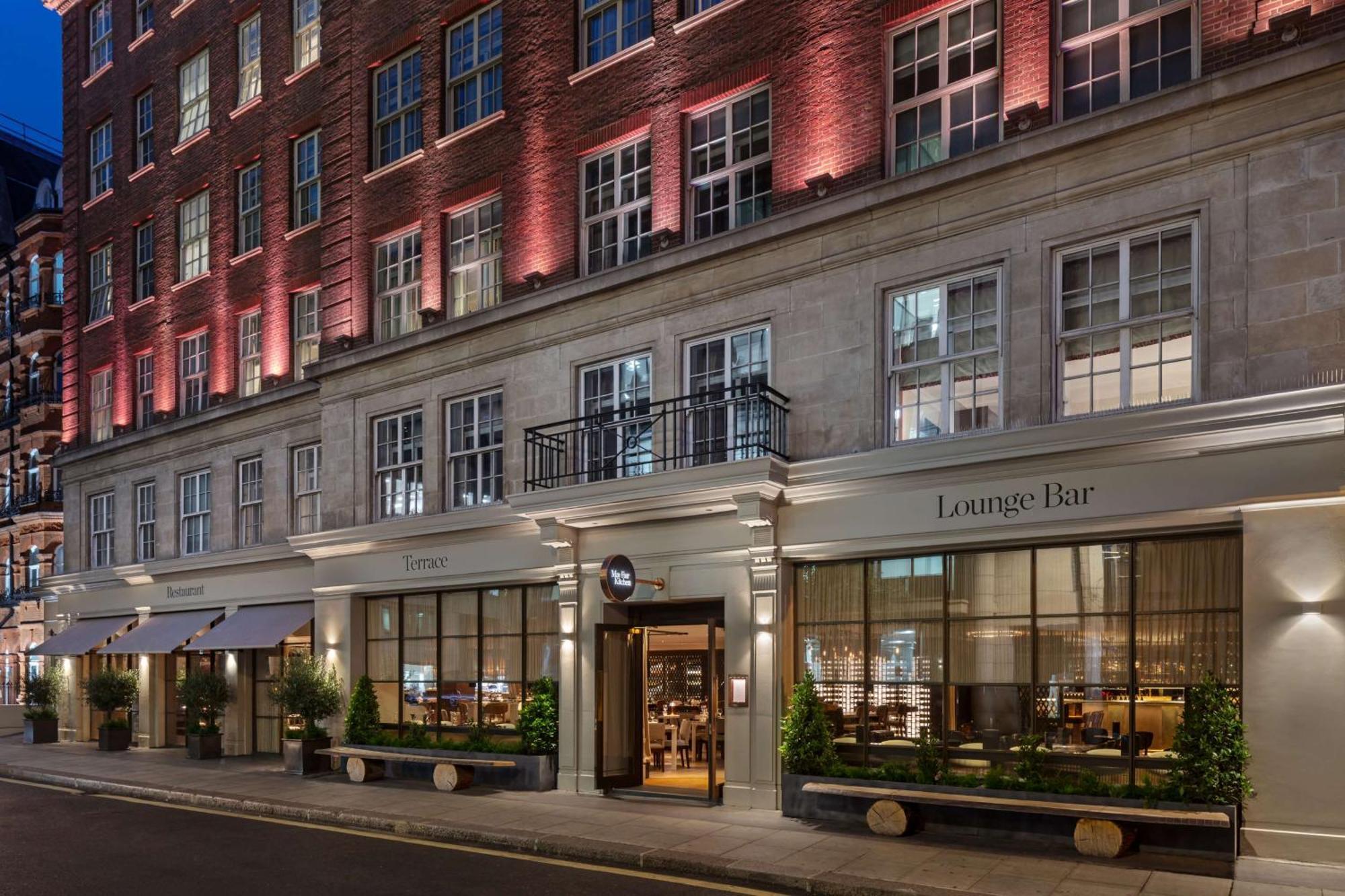 The May Fair, A Radisson Collection Hotel, Mayfair Londra Esterno foto The photo showcases a stylish building, likely a hotel or a high-end establishment. The facade features a mix of brick and stonework, and there are large windows that allow visibility into the lounge area. The entrance is marked by a sign indicating 