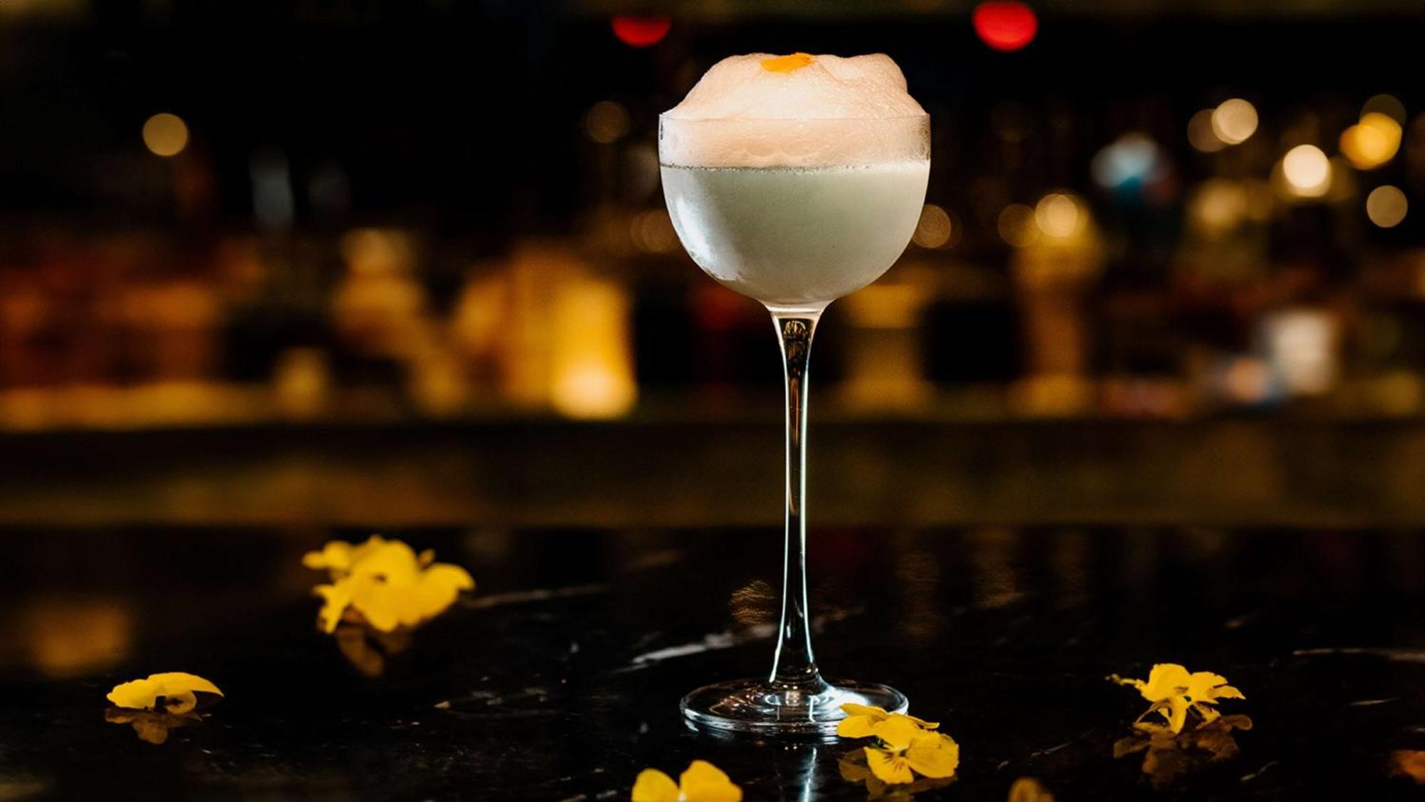 The May Fair, A Radisson Collection Hotel, Mayfair Londra Esterno foto The photo shows a stylish cocktail served in an elegant stemmed glass. The drink appears to be light in color, topped with a frothy layer, possibly a foam or whipped ingredient. Around the glass, there are yellow flower petals scattered on the surfac