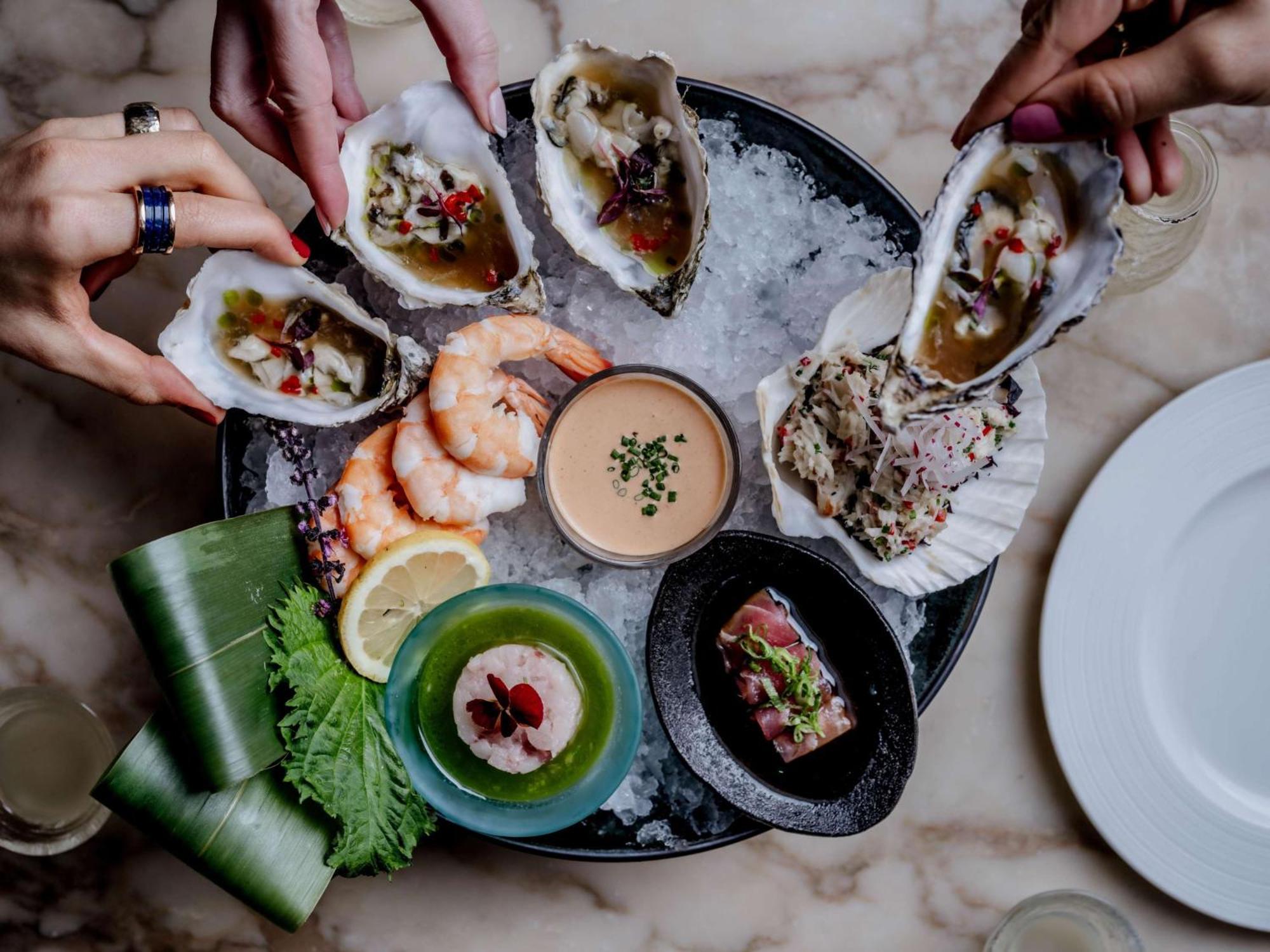 The May Fair, A Radisson Collection Hotel, Mayfair Londra Esterno foto The photo displays a seafood platter arranged beautifully on a round dish filled with ice. Various types of seafood are presented, including several open oysters topped with garnishes, shrimp, and a small dish of sauce in the center. Surrounding the 