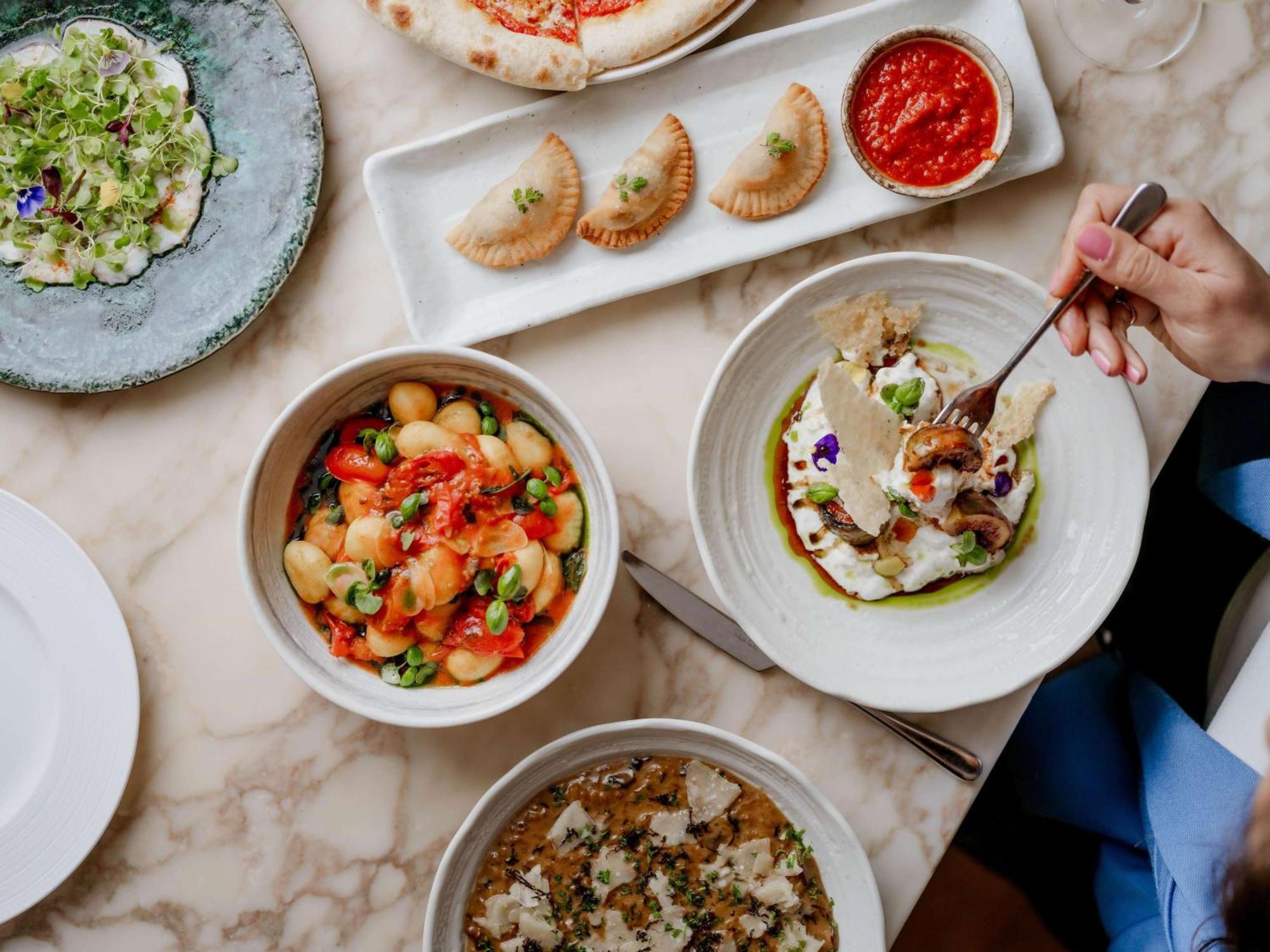 The May Fair, A Radisson Collection Hotel, Mayfair Londra Esterno foto The photo showcases a beautifully arranged table filled with various dishes. In the foreground, there are three bowls: one containing a colorful mix of gnocchi with vibrant toppings, another featuring a dish with what appears to be fish or seafood, g